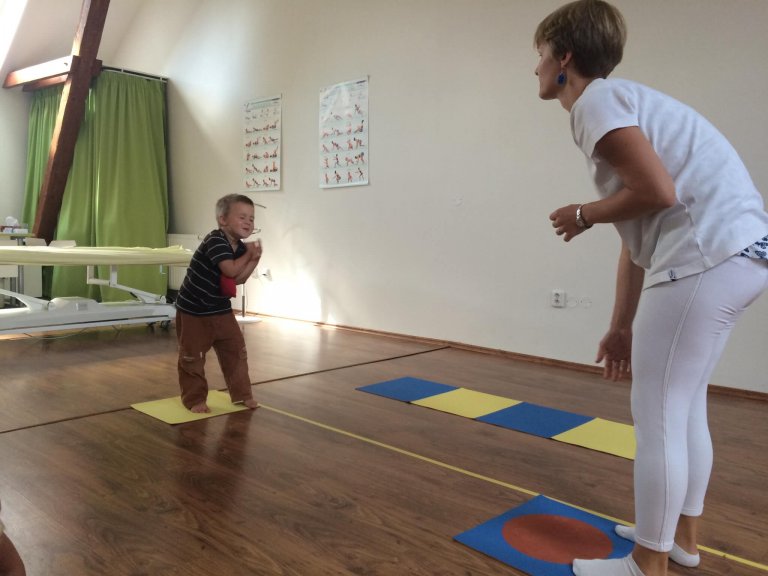 Batole prochází po barevných podložkách vedle terapeutky